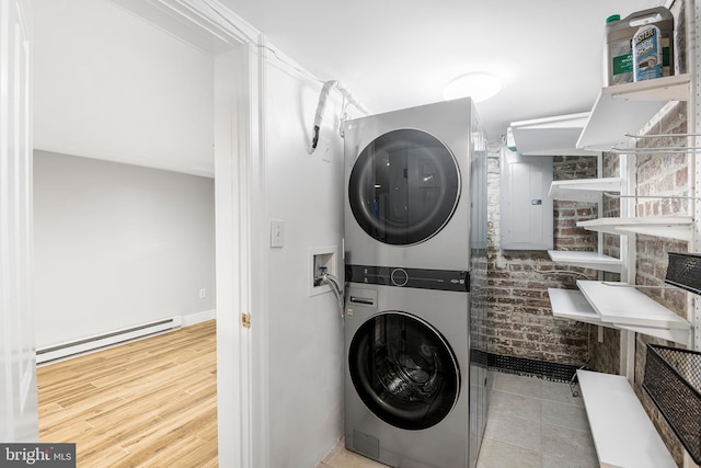 laundry area featuring brick wall, light hardwood / wood-style floors, stacked washer and clothes dryer, and a baseboard heating unit