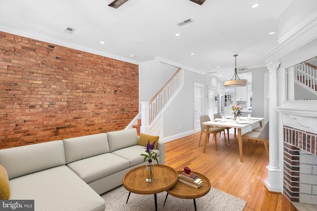 living room with a fireplace, light hardwood / wood-style flooring, crown molding, and brick wall