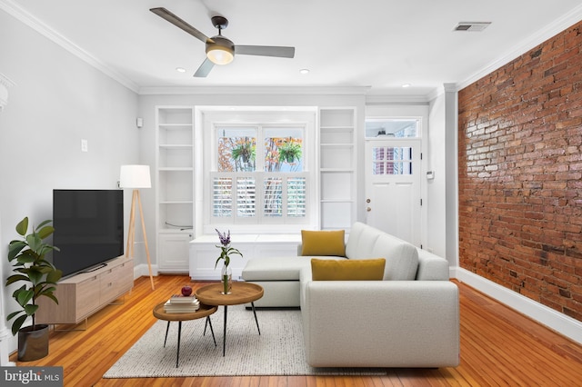 living room with ceiling fan, light hardwood / wood-style floors, crown molding, and brick wall