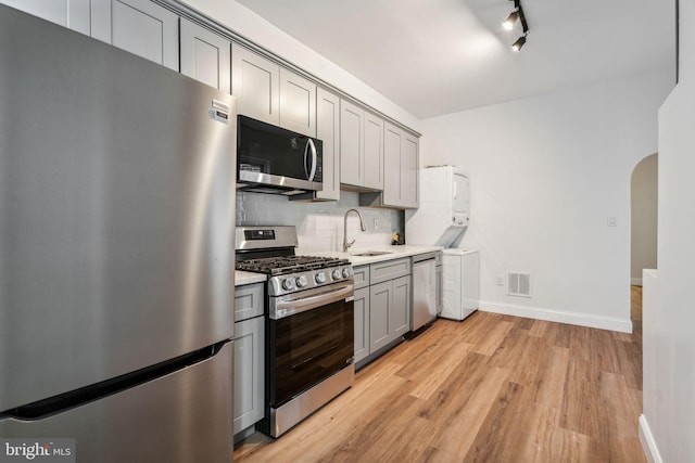 kitchen with stacked washer and clothes dryer, decorative backsplash, gray cabinetry, light wood-type flooring, and appliances with stainless steel finishes