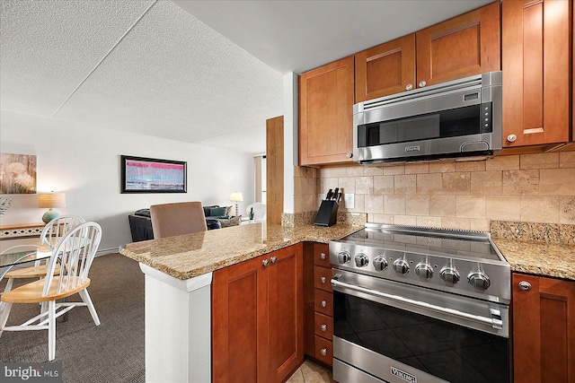 kitchen featuring stainless steel appliances, light stone counters, kitchen peninsula, a textured ceiling, and backsplash