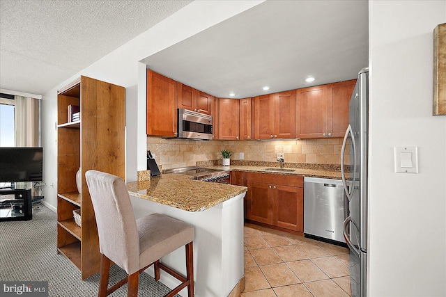 kitchen with kitchen peninsula, appliances with stainless steel finishes, a breakfast bar area, light tile patterned floors, and decorative backsplash