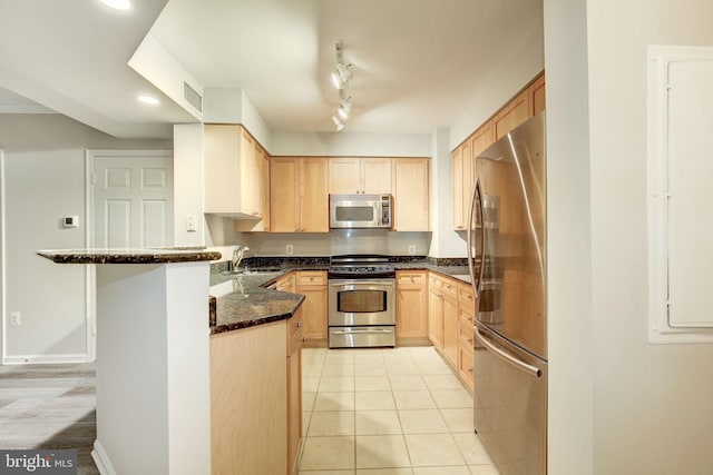 kitchen featuring sink, kitchen peninsula, dark stone counters, light brown cabinetry, and appliances with stainless steel finishes