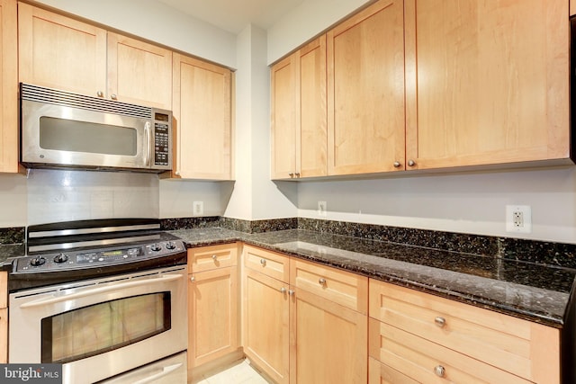 kitchen with light brown cabinetry, appliances with stainless steel finishes, and dark stone counters