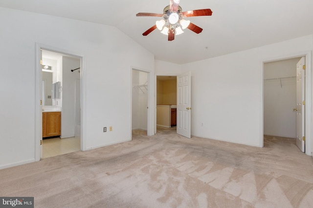 unfurnished bedroom with ceiling fan, ensuite bathroom, vaulted ceiling, a walk in closet, and light carpet