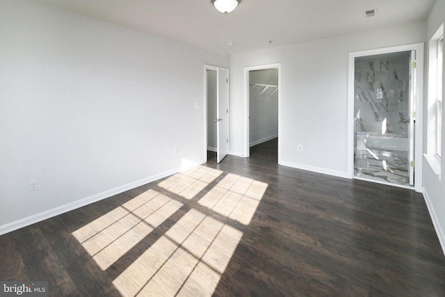 unfurnished bedroom featuring ensuite bathroom, dark hardwood / wood-style flooring, a spacious closet, and a closet