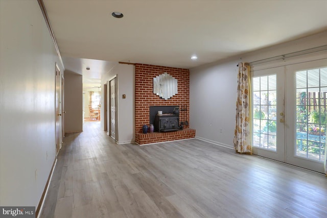 unfurnished living room with a wood stove, light wood-type flooring, and french doors