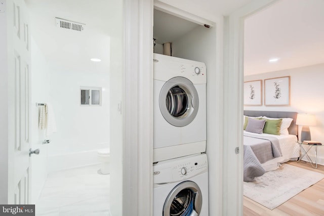 laundry room with light wood-type flooring and stacked washer / drying machine