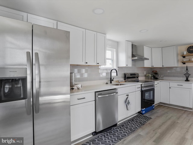 kitchen featuring stainless steel appliances, wall chimney range hood, decorative backsplash, white cabinets, and sink