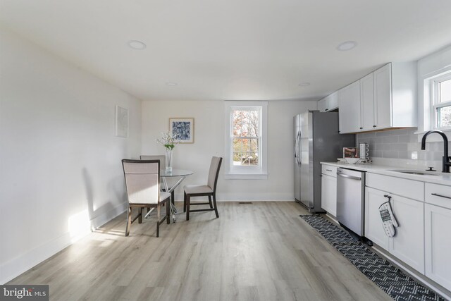 kitchen featuring a healthy amount of sunlight, stainless steel appliances, backsplash, white cabinetry, and sink