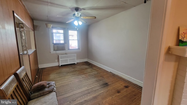 unfurnished room with dark hardwood / wood-style floors, radiator, wood walls, and ceiling fan