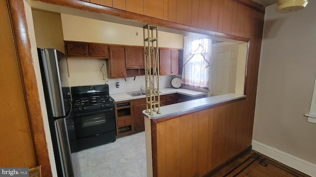 kitchen with sink, kitchen peninsula, stainless steel fridge, wood walls, and black range with gas cooktop