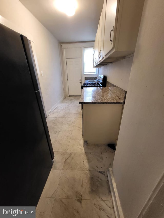 kitchen with dark stone counters, white cabinetry, and black fridge