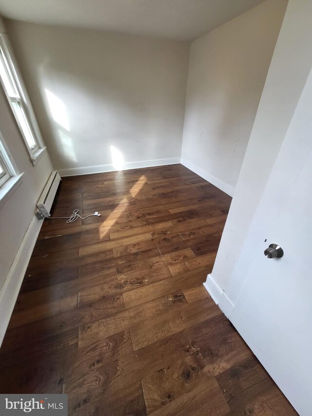 empty room with a baseboard heating unit and dark hardwood / wood-style flooring