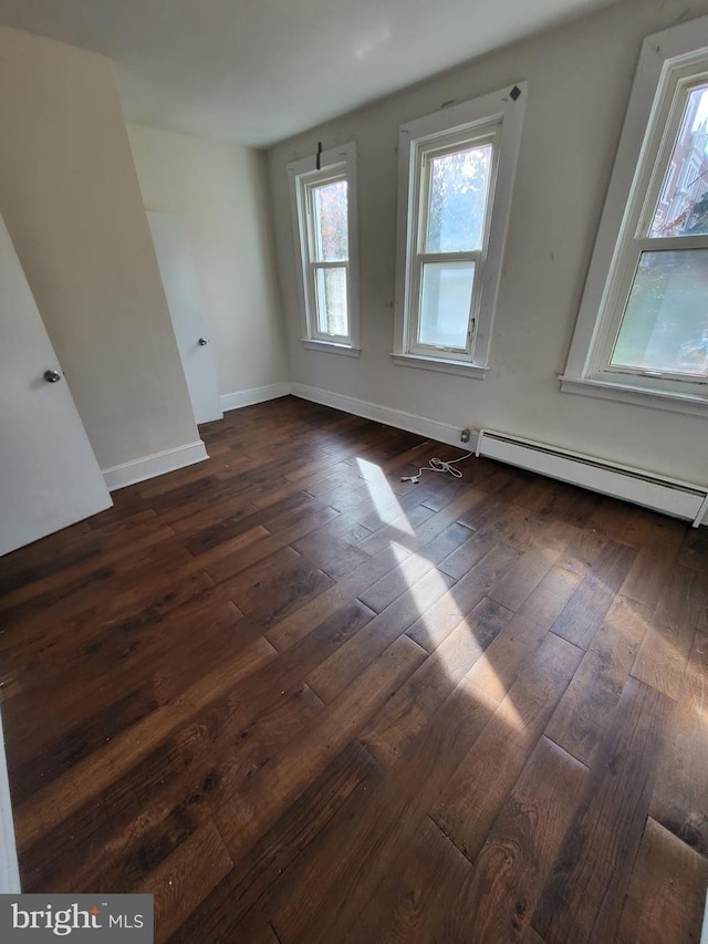 unfurnished room with baseboard heating and dark wood-type flooring