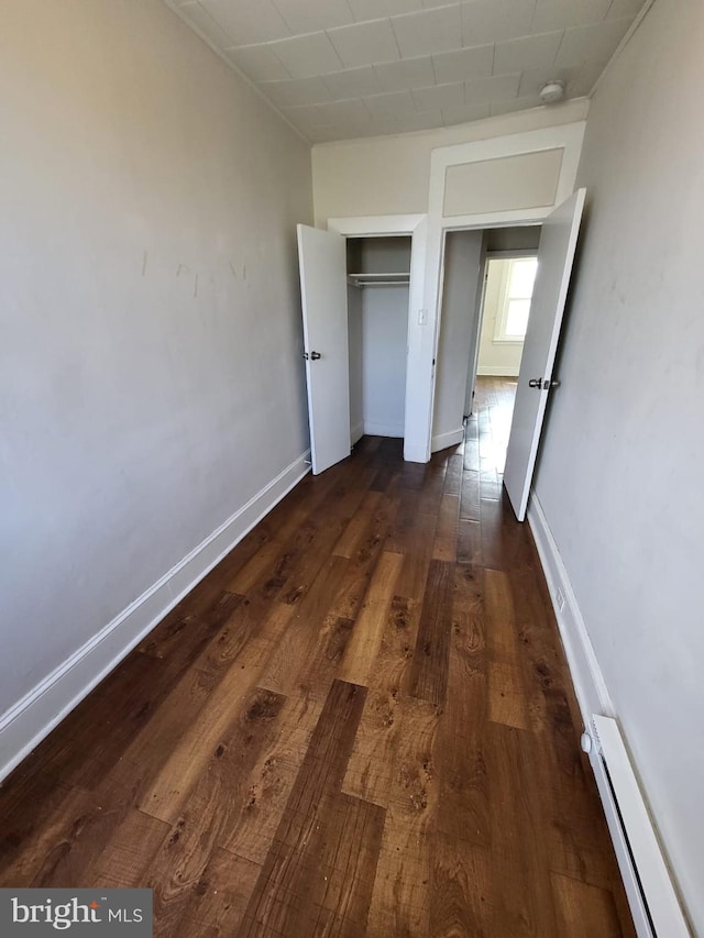 unfurnished bedroom featuring a baseboard heating unit, dark hardwood / wood-style flooring, and a closet