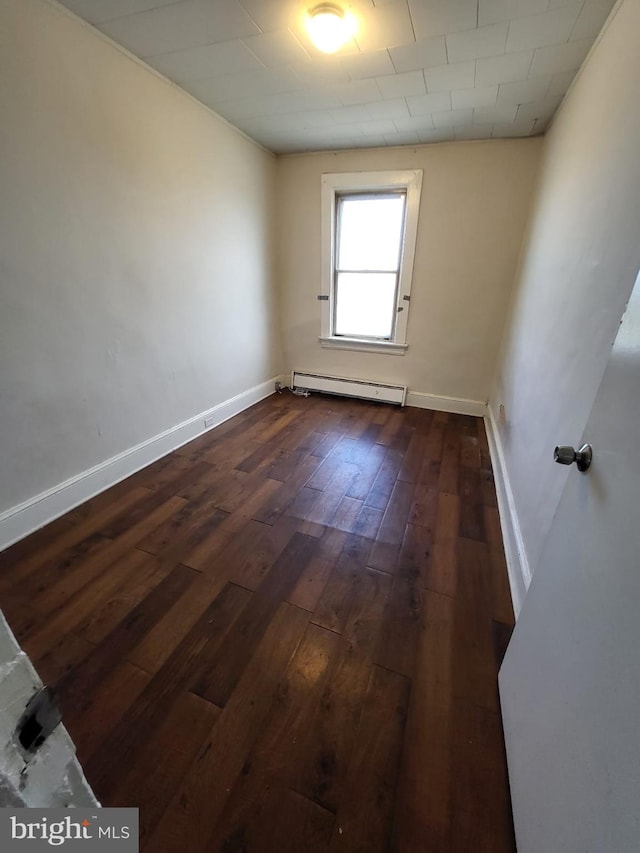 empty room featuring baseboard heating and dark wood-type flooring