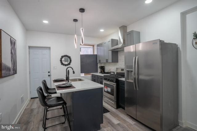 kitchen with appliances with stainless steel finishes, gray cabinetry, wall chimney exhaust hood, sink, and wood-type flooring