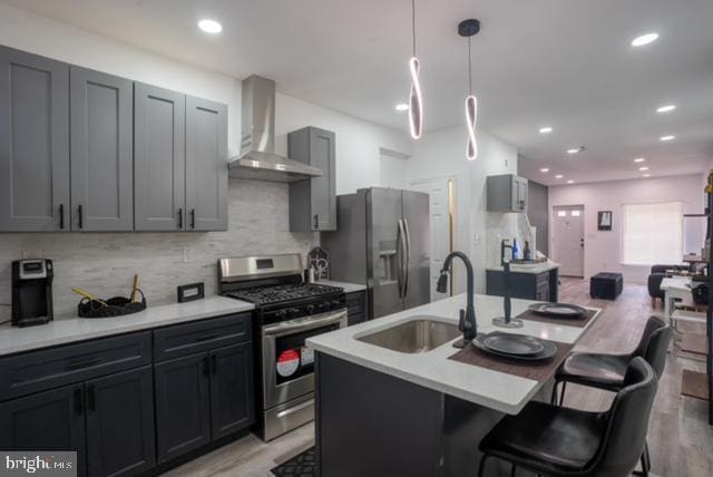 kitchen with a center island with sink, sink, light hardwood / wood-style flooring, wall chimney exhaust hood, and appliances with stainless steel finishes