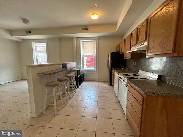 kitchen featuring a wealth of natural light, range with electric cooktop, light tile patterned floors, and a kitchen breakfast bar