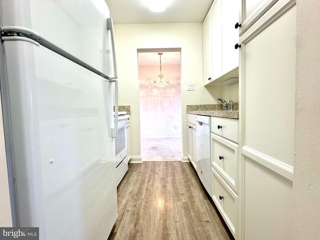 kitchen with hanging light fixtures, white appliances, white cabinetry, and light wood-type flooring