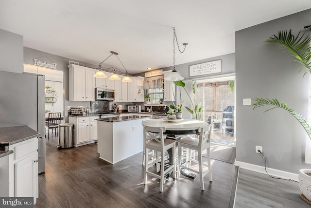 kitchen featuring white cabinets, appliances with stainless steel finishes, hanging light fixtures, and dark wood-type flooring