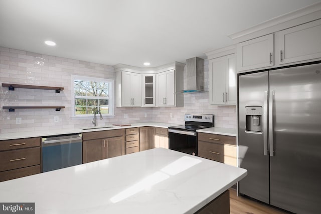 kitchen with stainless steel appliances, light hardwood / wood-style floors, sink, white cabinets, and wall chimney range hood