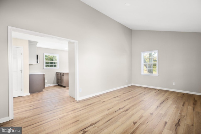 spare room featuring high vaulted ceiling, light wood-type flooring, and a healthy amount of sunlight