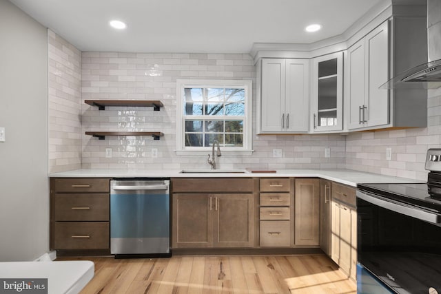 kitchen with wall chimney range hood, appliances with stainless steel finishes, backsplash, sink, and light hardwood / wood-style floors