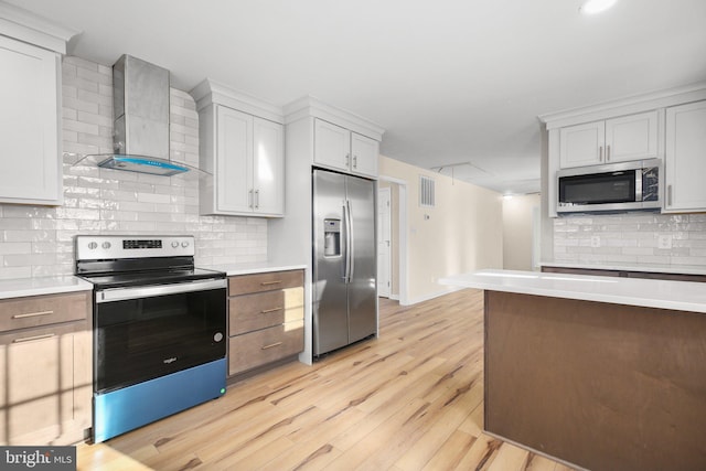 kitchen with white cabinetry, appliances with stainless steel finishes, wall chimney exhaust hood, and light hardwood / wood-style flooring