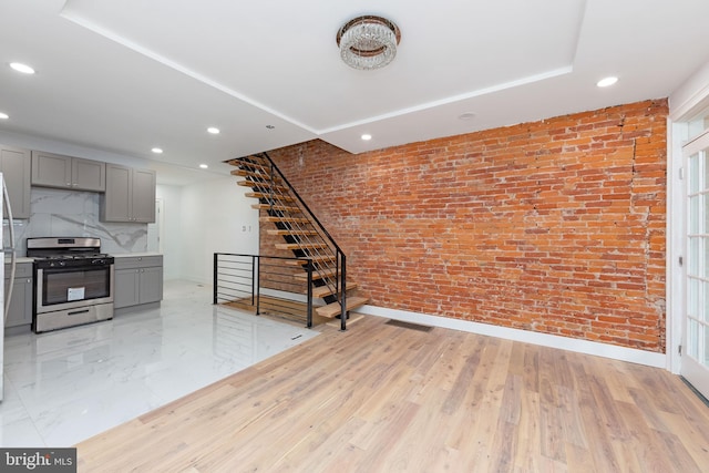 interior space with gray cabinets, stainless steel range oven, brick wall, and light hardwood / wood-style flooring