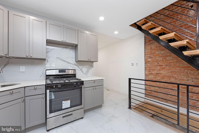 kitchen featuring backsplash, stainless steel gas range oven, and gray cabinets