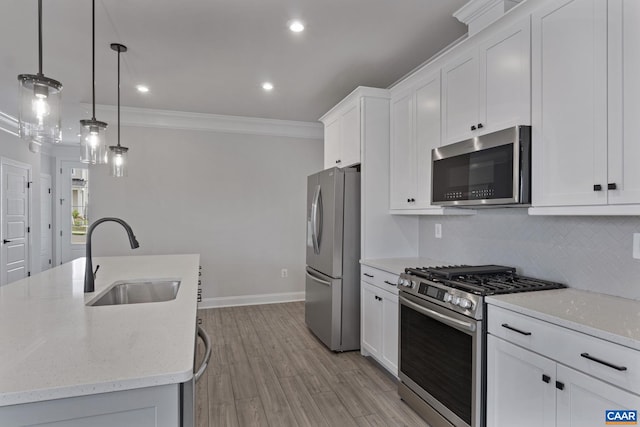 kitchen with light wood-type flooring, appliances with stainless steel finishes, pendant lighting, sink, and white cabinets