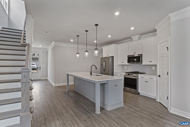 kitchen with a kitchen island with sink, stainless steel appliances, white cabinetry, decorative light fixtures, and light hardwood / wood-style flooring