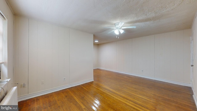 unfurnished room with radiator, hardwood / wood-style floors, wood walls, a textured ceiling, and ceiling fan