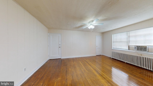 empty room with a textured ceiling, cooling unit, hardwood / wood-style flooring, and radiator