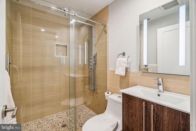 bathroom with toilet, vanity, tile walls, and a shower with door