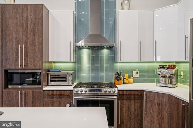 kitchen with tasteful backsplash, dark brown cabinets, wall chimney range hood, white cabinetry, and appliances with stainless steel finishes