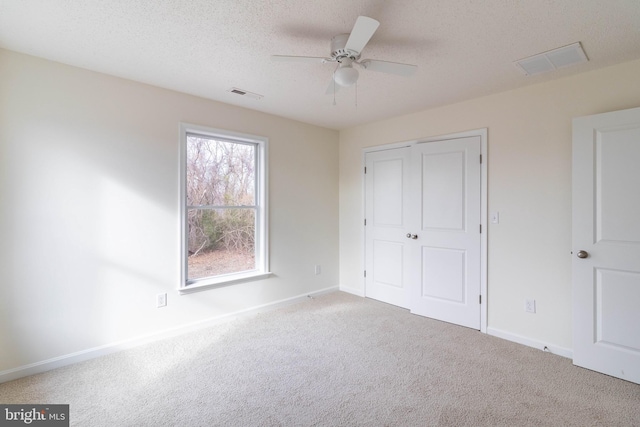 unfurnished bedroom with a textured ceiling, ceiling fan, light carpet, and a closet