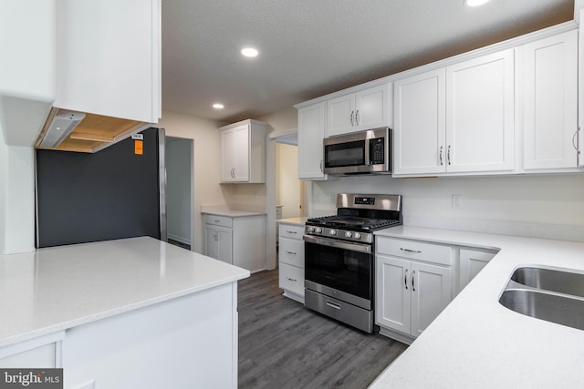 kitchen featuring sink, a textured ceiling, appliances with stainless steel finishes, dark hardwood / wood-style flooring, and white cabinetry