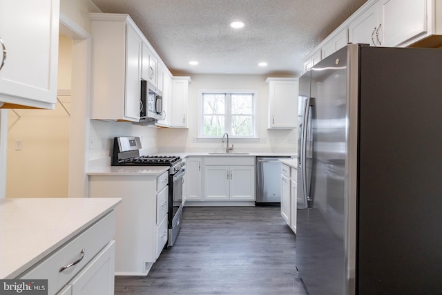 kitchen with appliances with stainless steel finishes, a textured ceiling, sink, white cabinets, and dark hardwood / wood-style floors