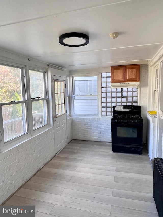 kitchen featuring black gas range oven, radiator, light hardwood / wood-style floors, and brick wall