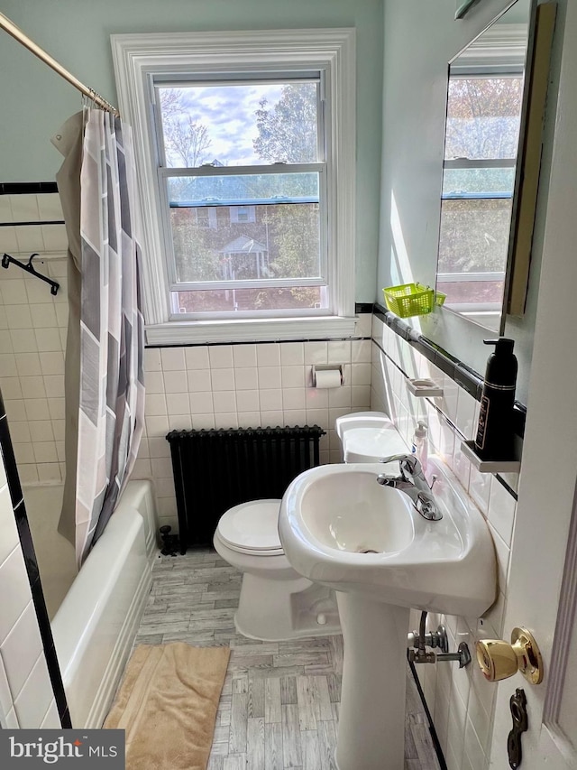 bathroom featuring hardwood / wood-style flooring, radiator, shower / bathtub combination with curtain, toilet, and tile walls