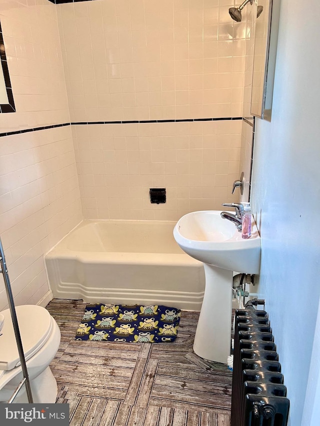 bathroom featuring toilet, radiator heating unit, tiled shower / bath, and tile walls