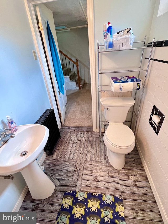 bathroom with wood-type flooring, radiator heating unit, tile walls, and toilet