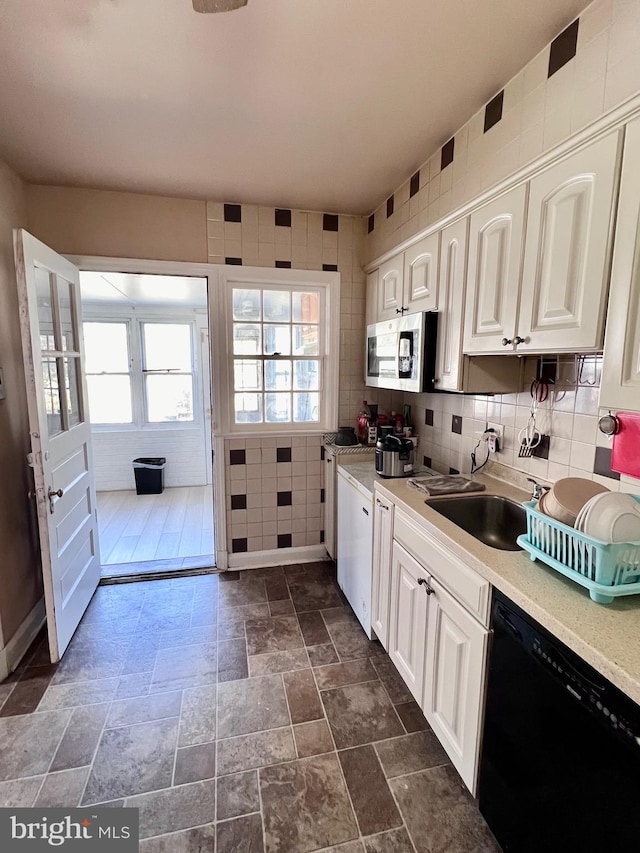 kitchen with black dishwasher, tile walls, white cabinetry, and backsplash