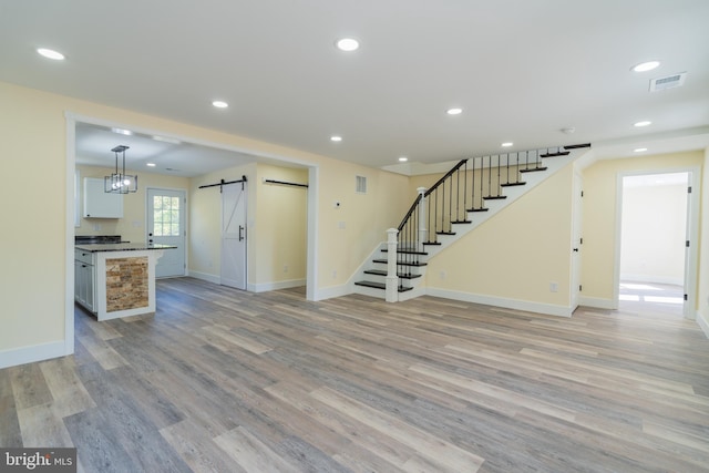 unfurnished living room with a barn door and light hardwood / wood-style flooring