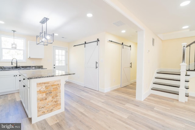 kitchen featuring dark stone counters, light hardwood / wood-style flooring, sink, white cabinets, and a center island