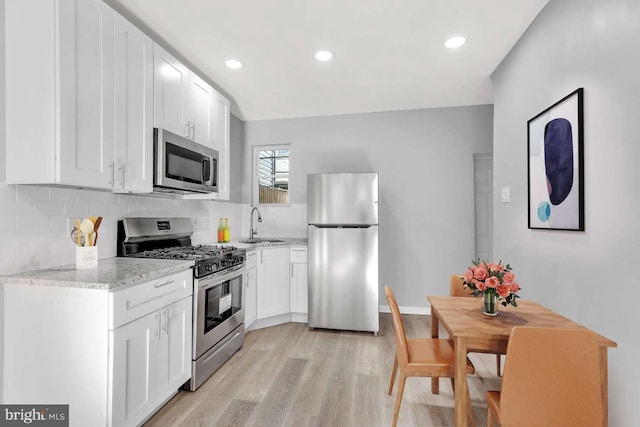 kitchen with stainless steel appliances, white cabinetry, sink, and light hardwood / wood-style flooring