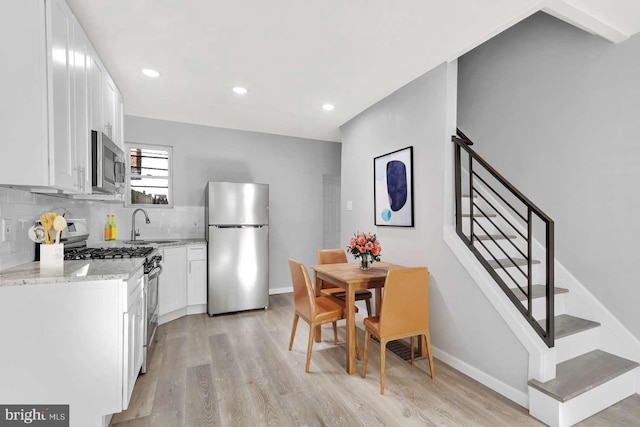 kitchen with light wood-type flooring, appliances with stainless steel finishes, light stone counters, and white cabinets